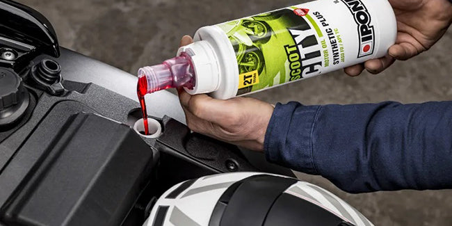 Motorcylist pouring Ipone Scoot City 2 stroke engine oil into his motorcycle engine.
